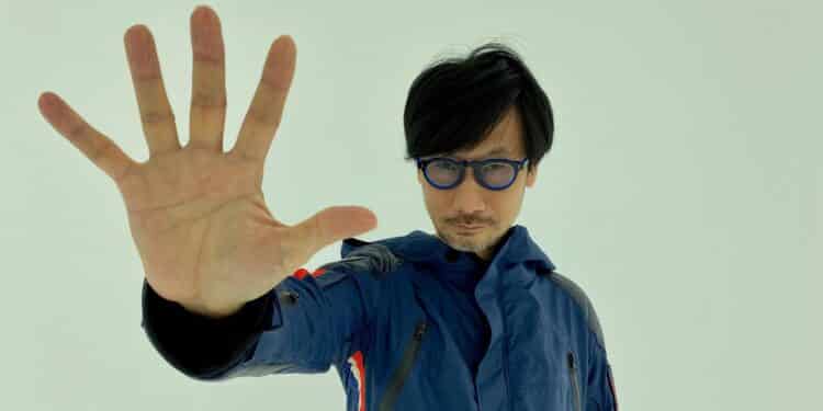 A photo of Hideo Kojima with his right hand out.